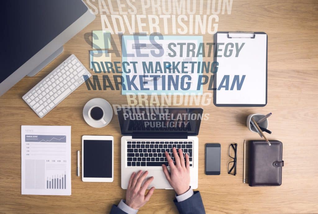 Widok z góry na profesjonalne biurko z nakładką słów związanych z marketingiem i strategią.