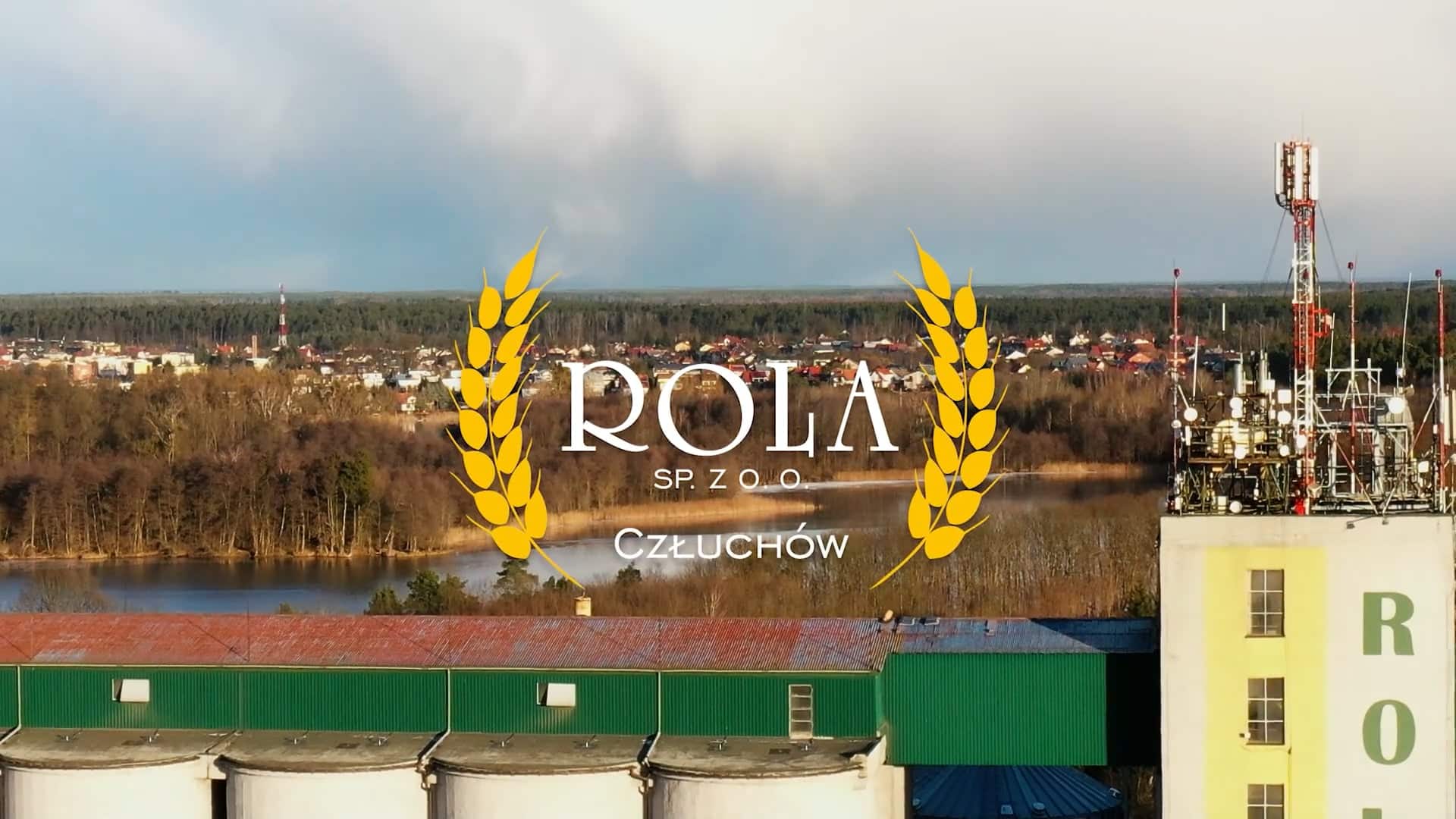 Na pierwszym planie fabryka z silosami, w tle jezioro i domy oraz napis "ROLA SP. Z O.O. Człuchów" z nałożoną grafiką pszenicy.