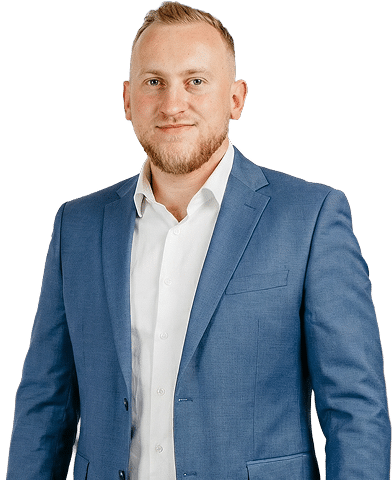 Mężczyzna z krótkimi blond włosami i brodą, ubrany w jasnoniebieską marynarkę i białą koszulę, stoi na białym tle.