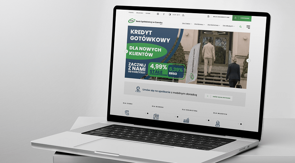 Laptop wyświetlający stronę główną witryny bankowej, zawierającą reklamę oferty pożyczki gotówkowej skierowanej do nowych klientów, ze szczegółami oprocentowania i banerem przedstawiającym osoby wchodzące do budynku.